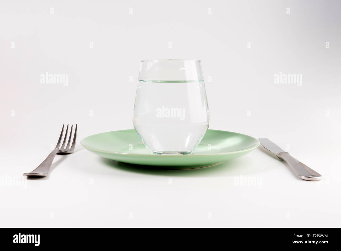 Verre d'eau dans une assiette avec fourchette et couteau isolé sur fond  blanc Photo Stock - Alamy