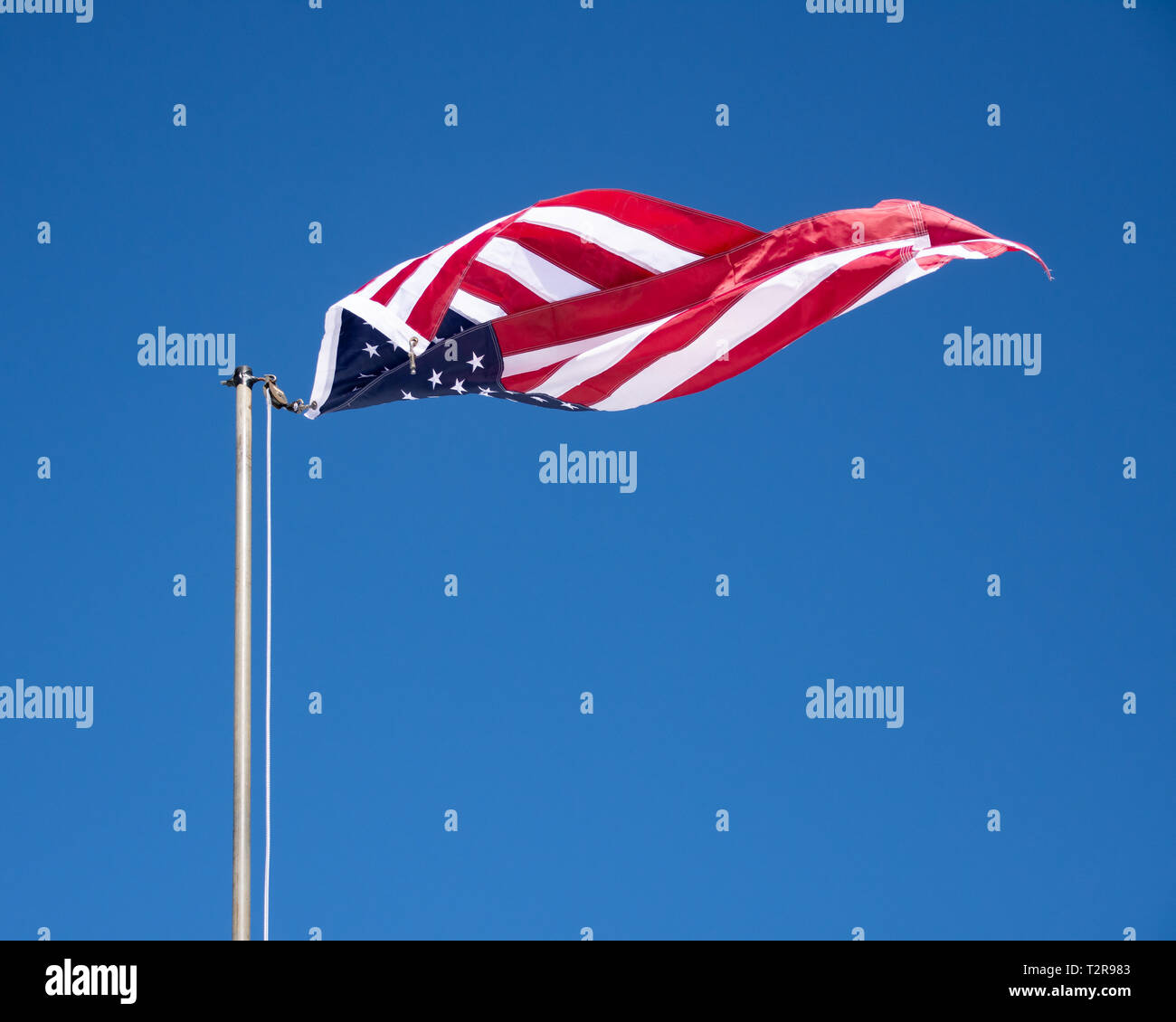 Un drapeau américain détaché de la ligne se tordre dans le vent contre un ciel bleu clair. Banque D'Images