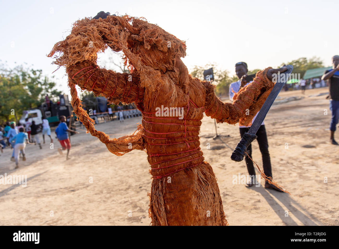 JANJANBUREH, la Gambie (19/01/2019) - Le Ifangbondi menace la foule avec une machette, quoique de manière ludique, alors que le soleil se couche sur le terrain du festival Janjanbureh. Le Festival Janjanbureh Kankurang fait partie d'efforts conjoints de l'UE au Fonds d'affectation spéciale d'urgence pour l'Afrique et le projet d'autonomisation des jeunes Gambiens pour stimuler le tourisme à Janjanbureh. En préservant et en célébrant le patrimoine culturel de l'Kankurang, c'est la création de nouvelles possibilités économiques pour les jeunes Gambiens sous la forme d'une augmentation du tourisme. Banque D'Images