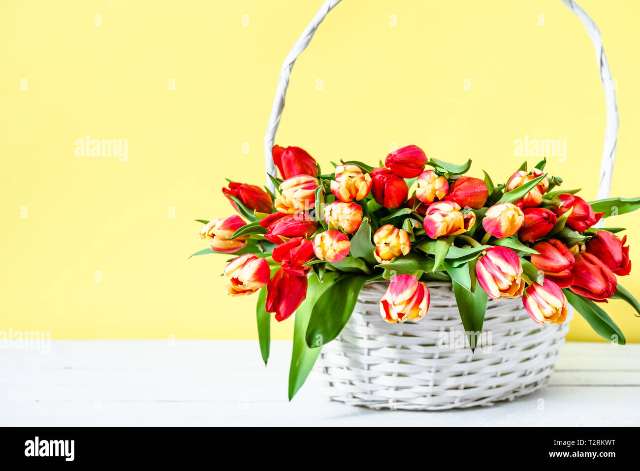 Panier avec bouquet de tulipe. Pâques Printemps fleurs sur fond jaune. Cadeau de fête des mères. Banque D'Images