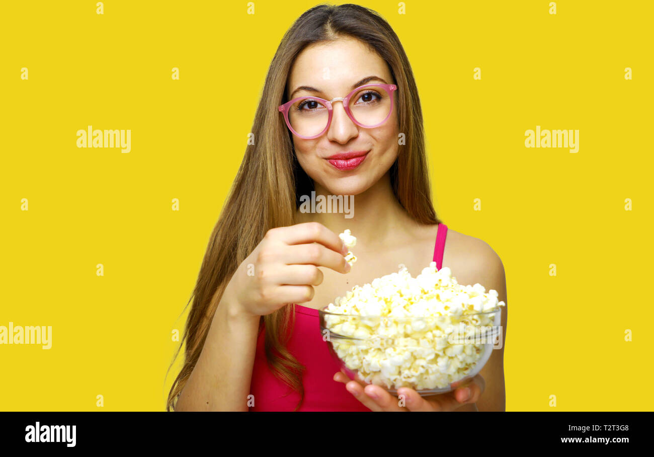 Fille avec émotion positive holding pop corn et regarder film comique isolé sur fond jaune studio portrait Banque D'Images