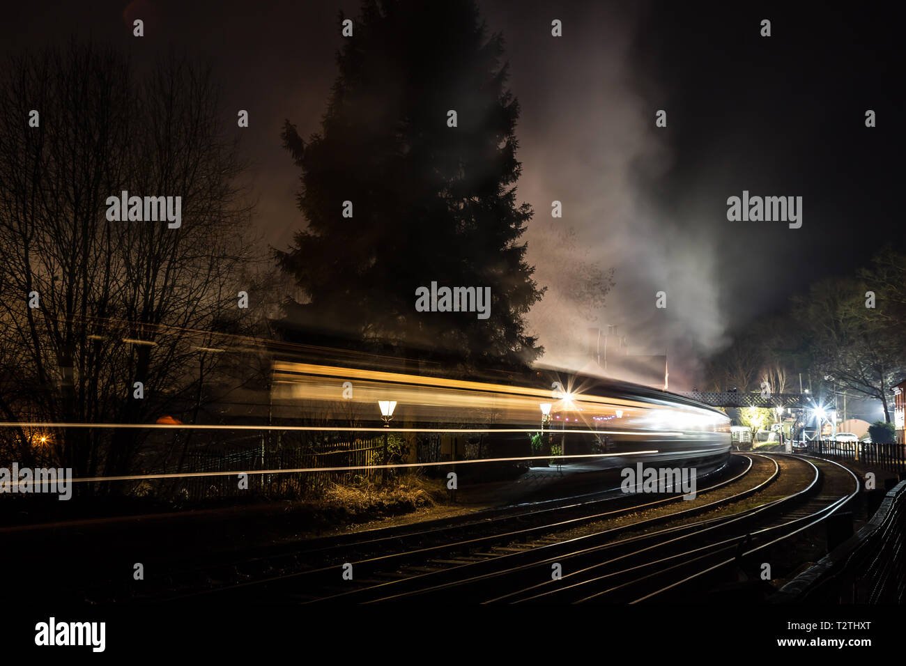 Train à vapeur et voitures qui se déplacent dans l'atmosphère et traversent la gare d'époque la nuit dans l'obscurité. Flou de mouvement rapide. Vitesse de concept. Banque D'Images