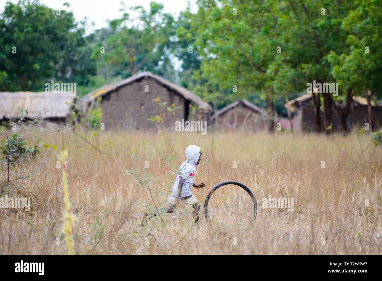 Garçon malawien chasse roue de bicyclette à travers son village Banque D'Images