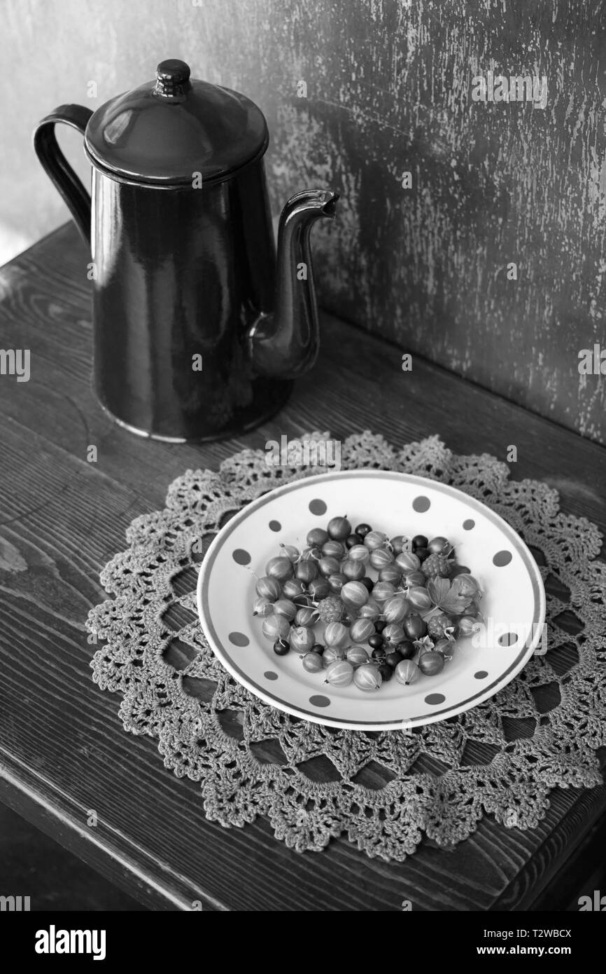 Vintage coffee pot émaillé et l'assiette de fruits de jardin sur la serviette décorative en bonneterie. Nature morte noir et blanc Banque D'Images