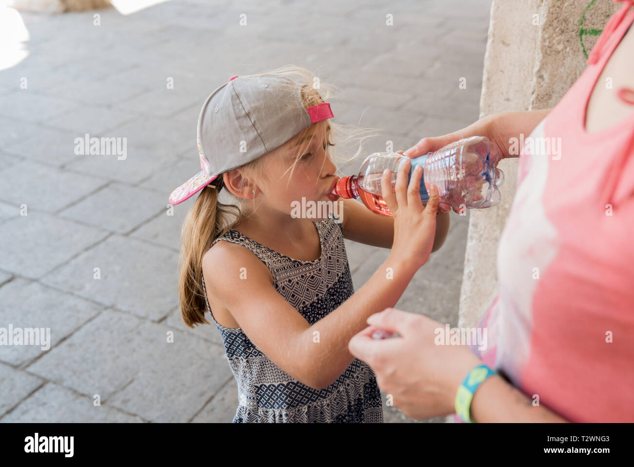 Portrait d'un enfant avec un cap de boire une bouteille d'eau au cours d'une chaude journée d'été. Le donner à elle par sa mère Banque D'Images