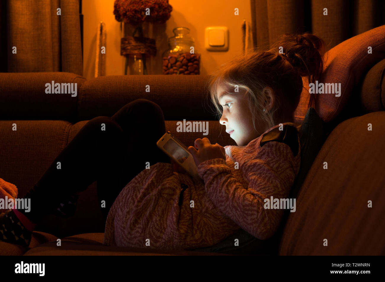 Portrait of a cute girl en utilisant un smartphone, reposant sur un canapé-l Banque D'Images