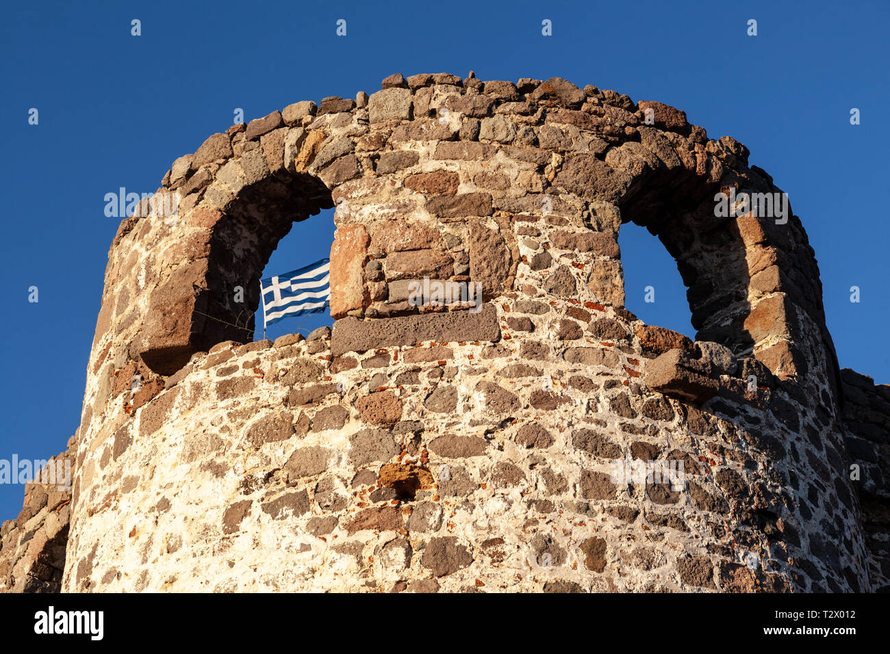 Château de Molyvos, île de Lesvos, Grèce et le drapeau grec agitant comme arrière-plan par le biais d'une de ses lacunes. Banque D'Images