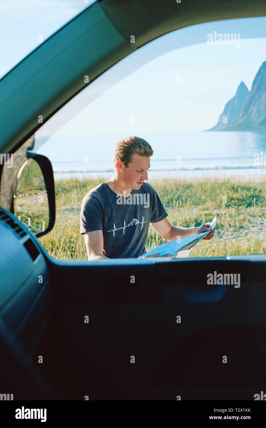 Un portrait d'emplacement d'un jeune homme de la carte lisant et planification de l'itinéraire assis à côté de sa voiture à la côte - sur la route - vanlife - carte papier - déplacement Banque D'Images