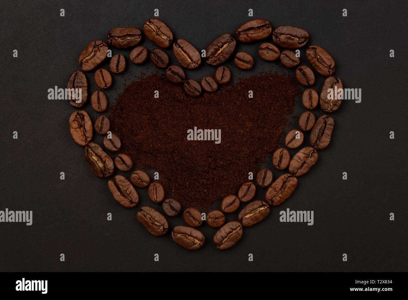 Les grains de café torréfiés placés dans une forme de coeur sur fond noir Banque D'Images