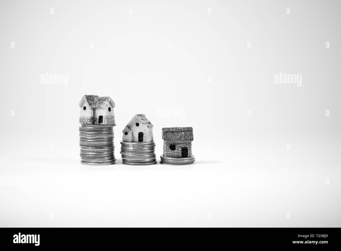 Maisons miniatures sur le dessus des piles de pièces de monnaie pour représenter les différences de prix Banque D'Images