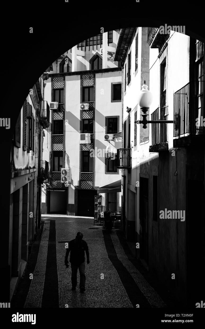 Rue arrière ruelles de Madère. Un vieil homme marche dans l'ombre d'une arcade. Banque D'Images