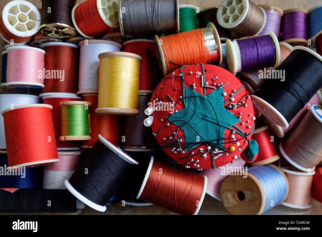 Une tomate pin cushion avec bobines de fil coloré dans un kit de couture. Banque D'Images