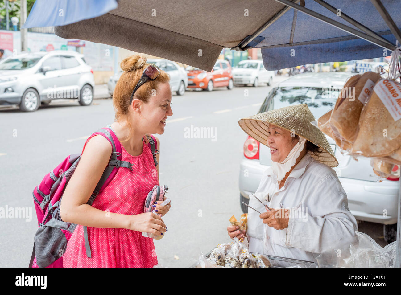 Nha Trang, Vietnam - Mai 5, 2018 : un voyageur européen solo et un dessert, un vendeur de rue dame vietnamienne dans un chapeau conique d'Asie Banque D'Images