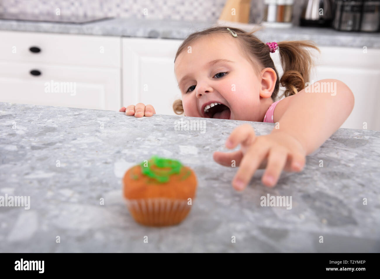 Smiling cute girl's Hand Reaching For Cupcake sur compteur de cuisine Banque D'Images