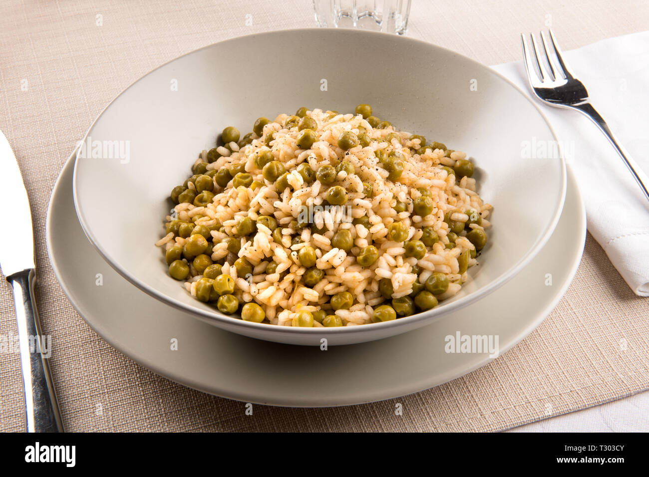 Assiette du traditionnel Risi e Bisi du Veneto, Italie faite avec stock, le riz, les assaisonnements et les pois verts frais, servi à table avec des ustensiles Banque D'Images