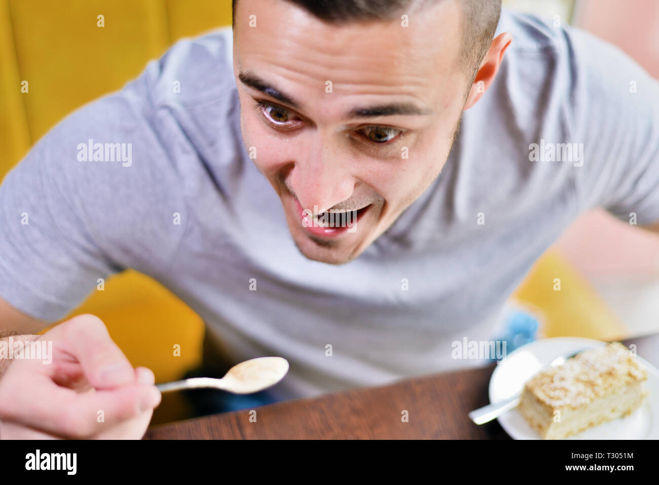 Jeune mec drôle dans le café. homme mange avec une cuillère. sur la table de gâteau soucoupe Banque D'Images