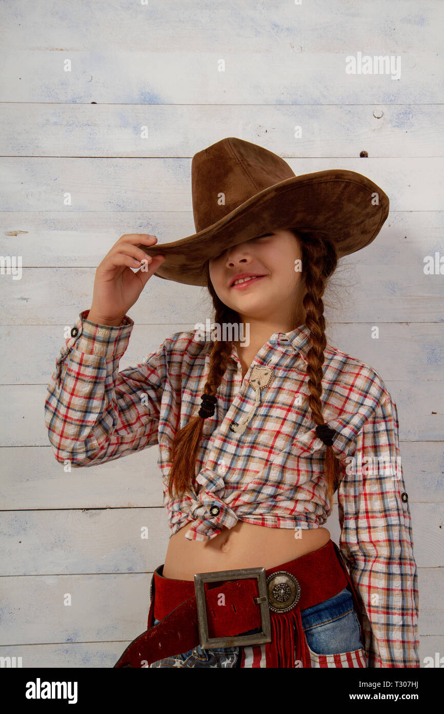Petite fille dans un chapeau de cow-boy à larges bords et des vêtements traditionnels posant sur un léger fond de bois Banque D'Images