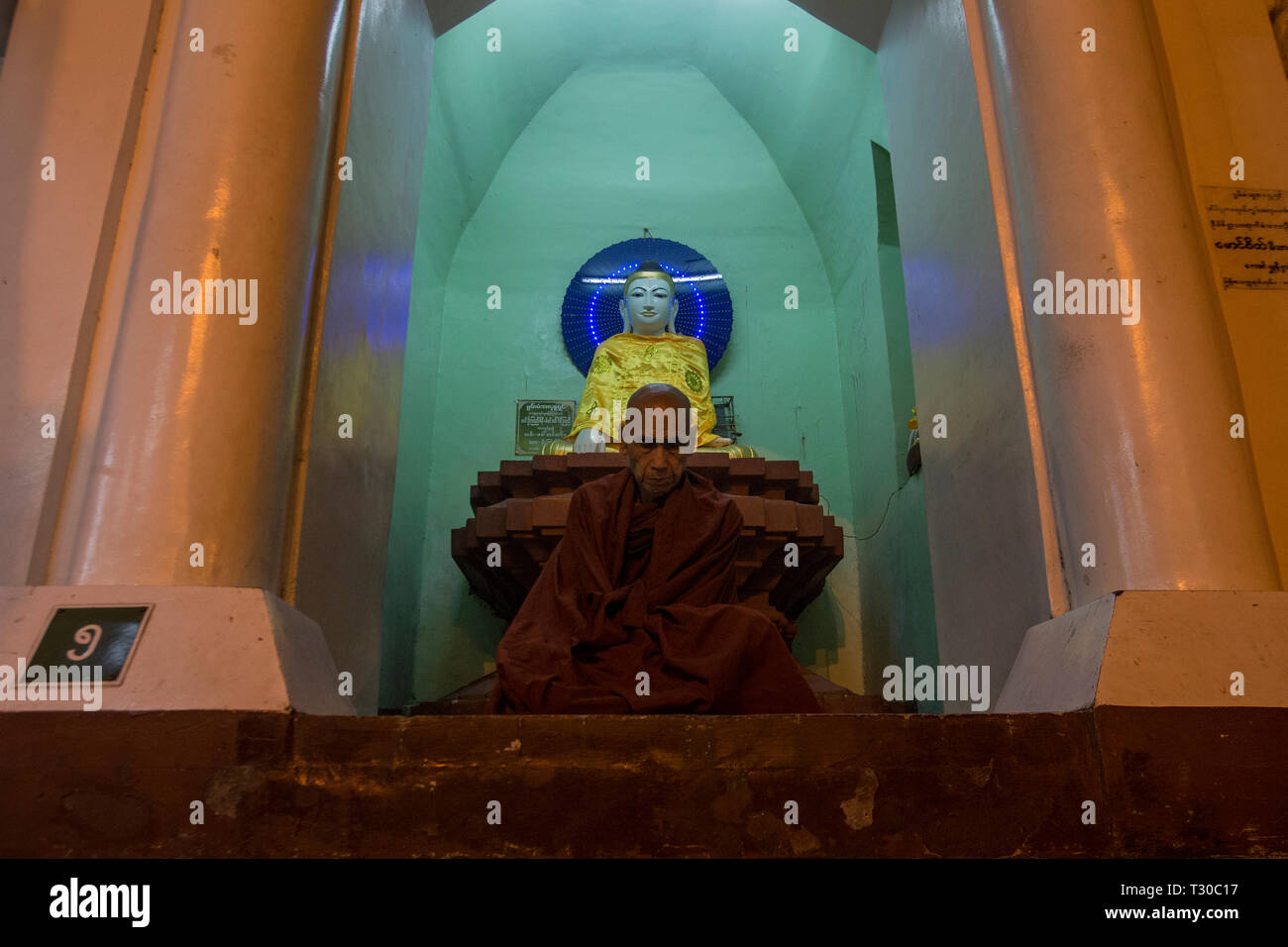 Un moine bouddhiste méditant devant un lieu de culte à la pagode Shwedagon, Yangon, Myanmar (Birmanie). Banque D'Images
