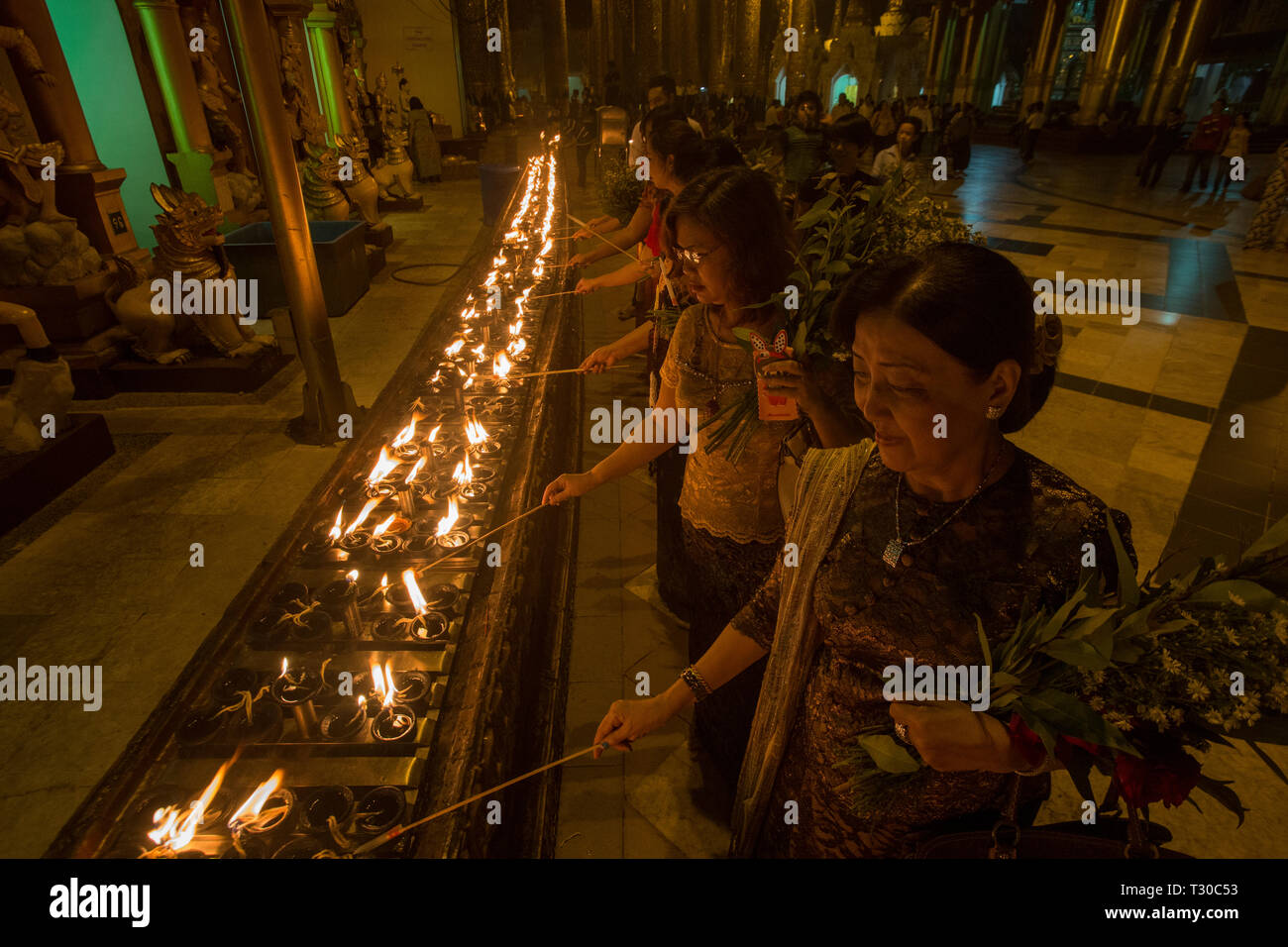 Les dévots bouddhistes birmans lampes à huile de l'éclairage à la pagode Shwedagon, Yangon, Myanmar (Birmanie). Banque D'Images