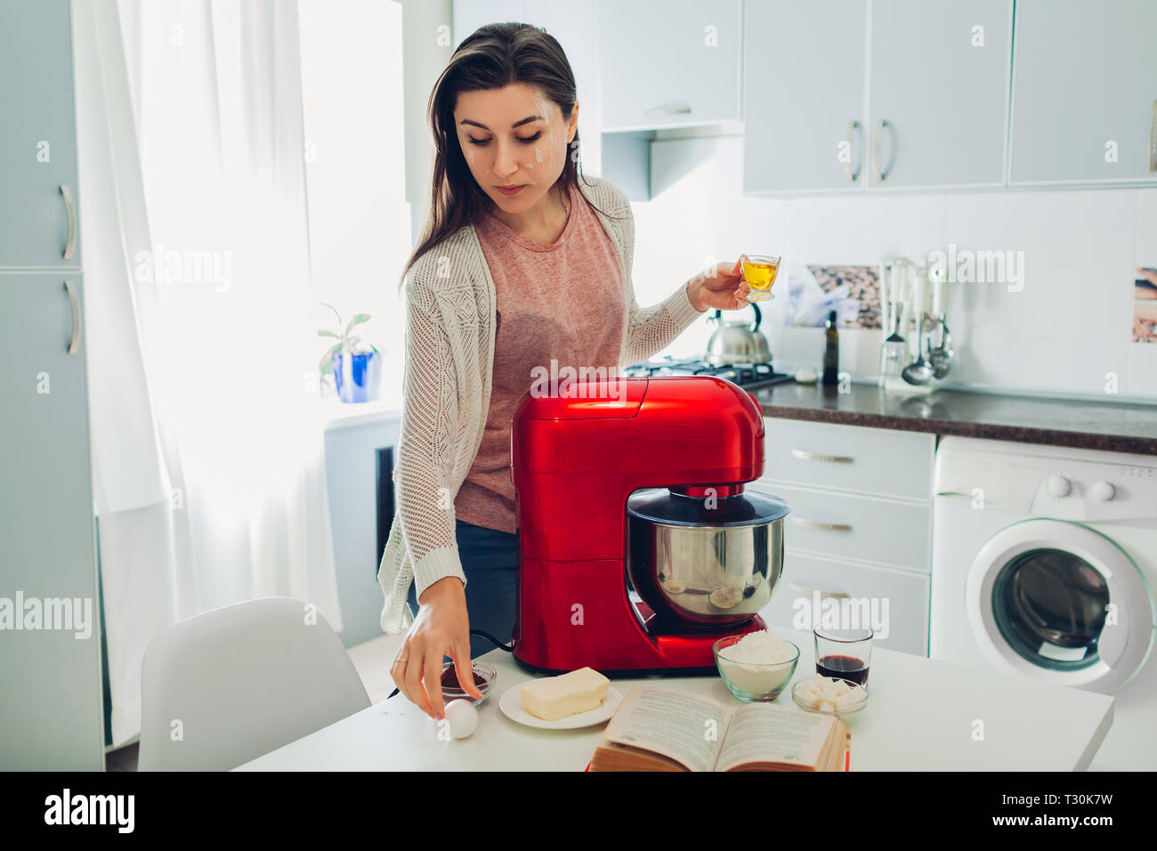 Jeune femme au foyer pie cuisine selon fiche de livre culinaire. Femme à l'aide de processeur de nourriture sur la cuisine à la maison. Banque D'Images