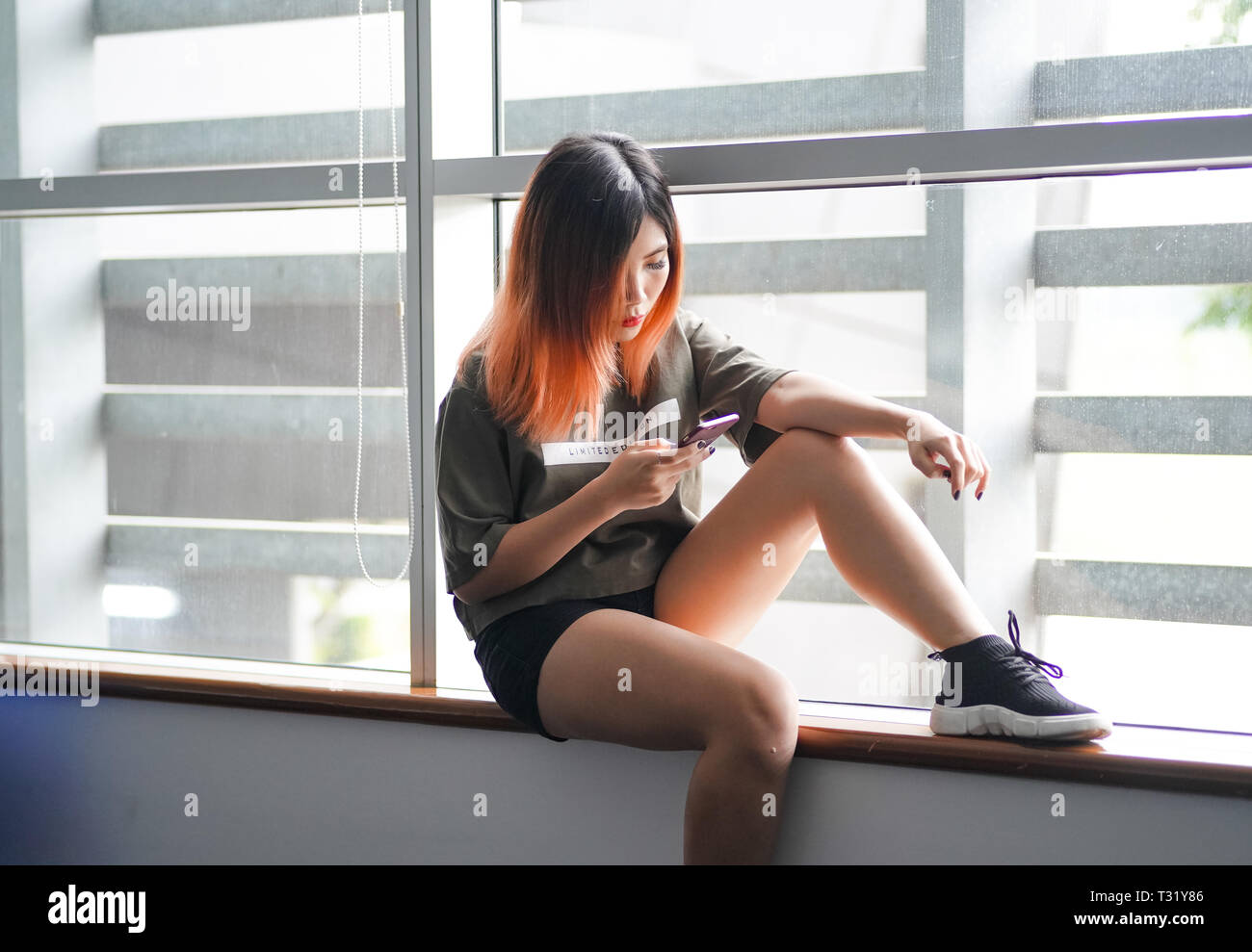 Highschool asiatique fille assise par la fenêtre using smartphone Banque D'Images