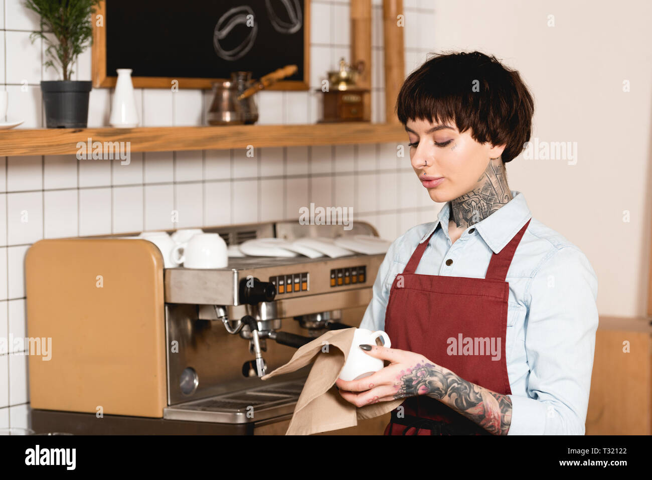 Belle tasse essuyage barista tout en se tenant près de la machine à espresso in coffee shop Banque D'Images