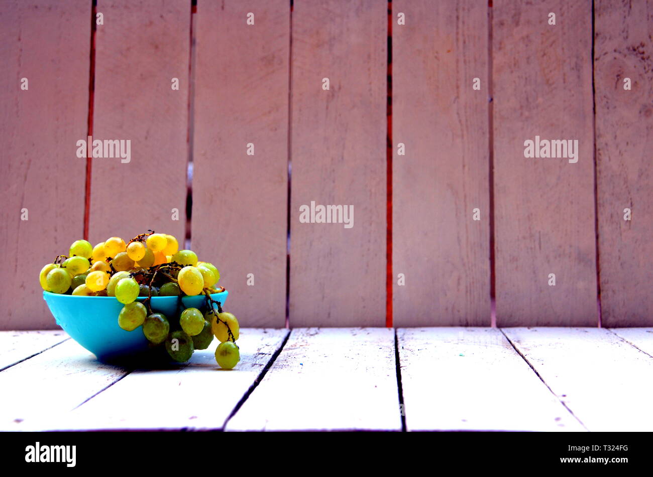 Bodegon d'une grappe de raisins dans un bol bleu sur une palette en bois blanc Banque D'Images