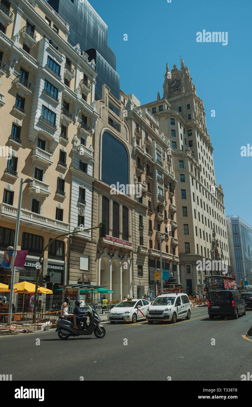 De vieux bâtiments avec des boutiques sur rue animée avec des gens et des voitures, dans une journée ensoleillée à Madrid. Capitale de l'Espagne avec dynamisme et vie culturelle intense. Banque D'Images