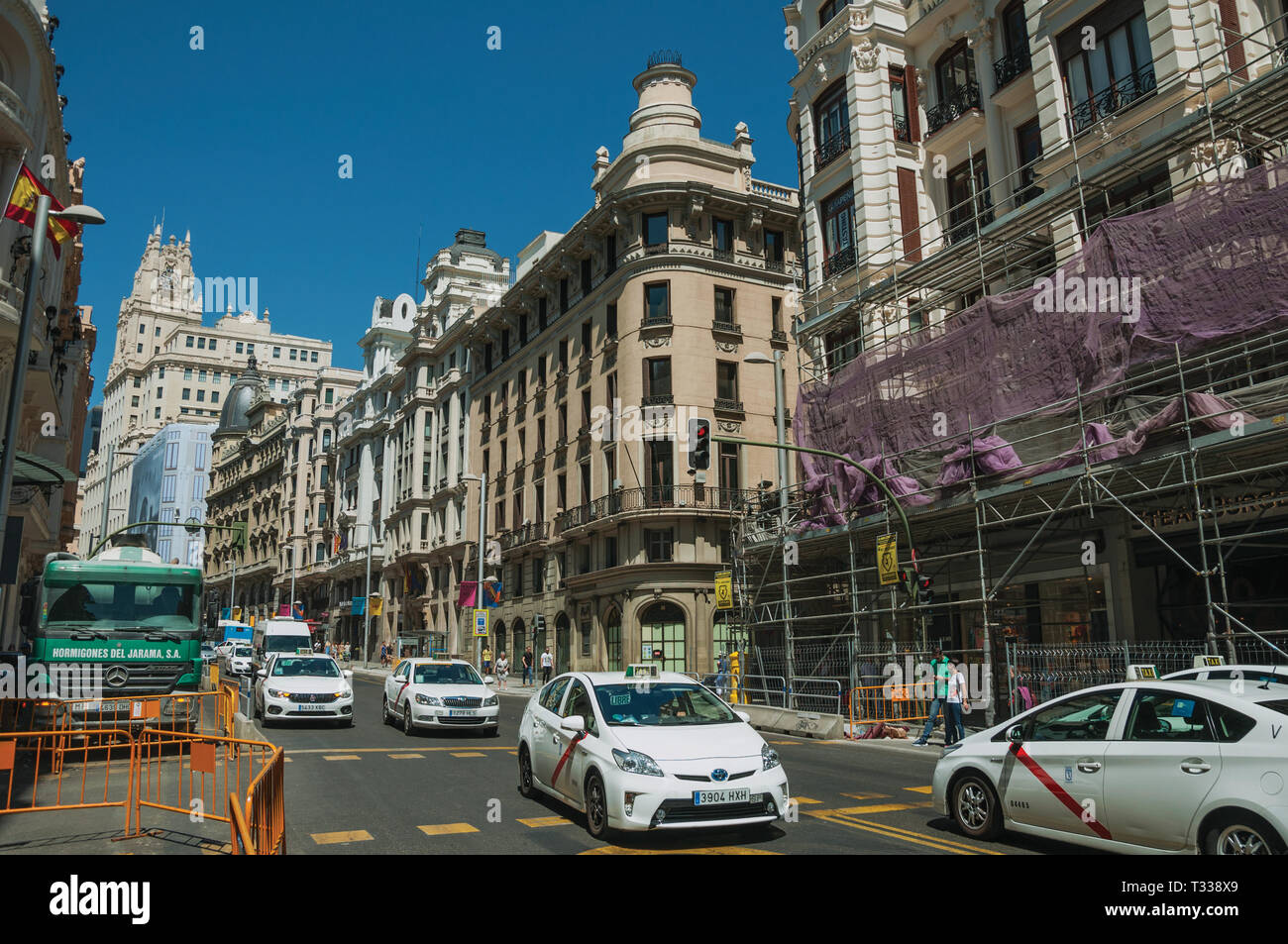 De vieux bâtiments avec des boutiques sur rue animée avec des gens et des voitures, dans une journée ensoleillée à Madrid. Capitale de l'Espagne avec dynamisme et vie culturelle intense. Banque D'Images