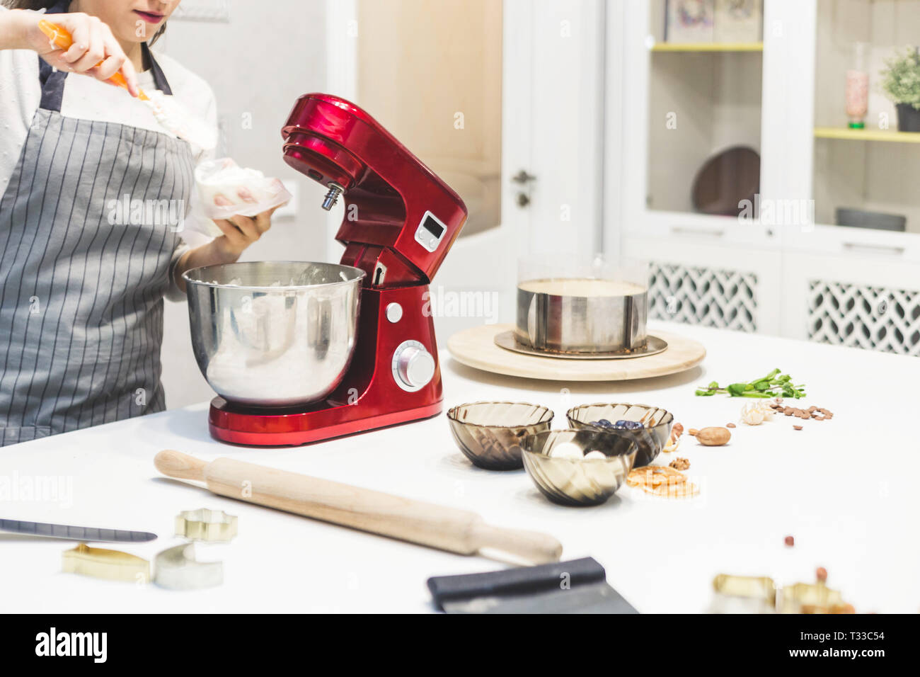 Jeune femme pâtissier bat la crème dans un bol en métal rouge dans un mélangeur électrique. Le concept de pâtisserie maison, la cuisine Banque D'Images