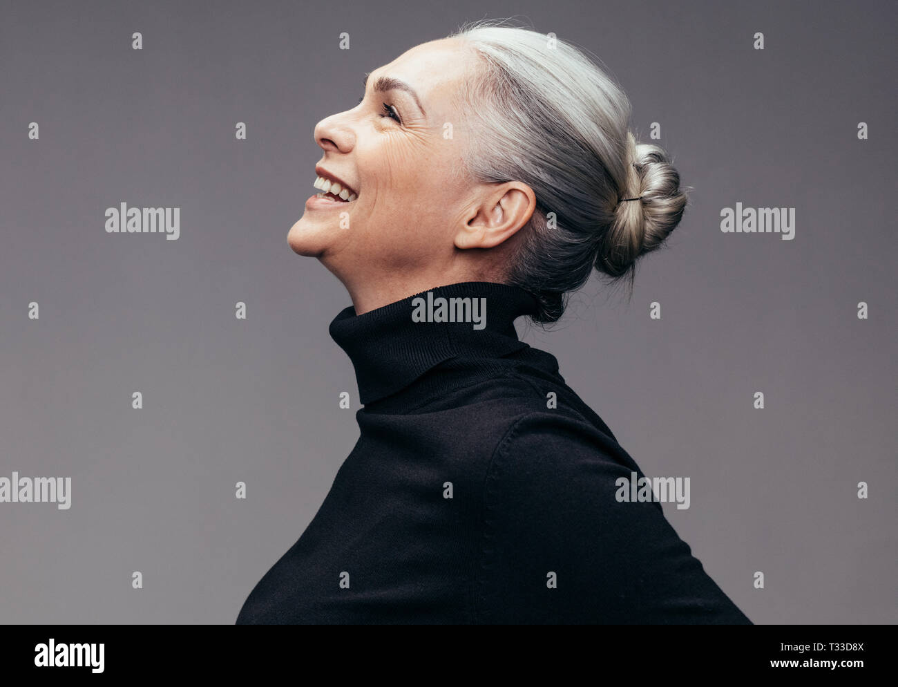 Vue latérale du senior woman laughing sur fond gris. Vue de profil de femme mature en noir les occasionnels à heureux Banque D'Images