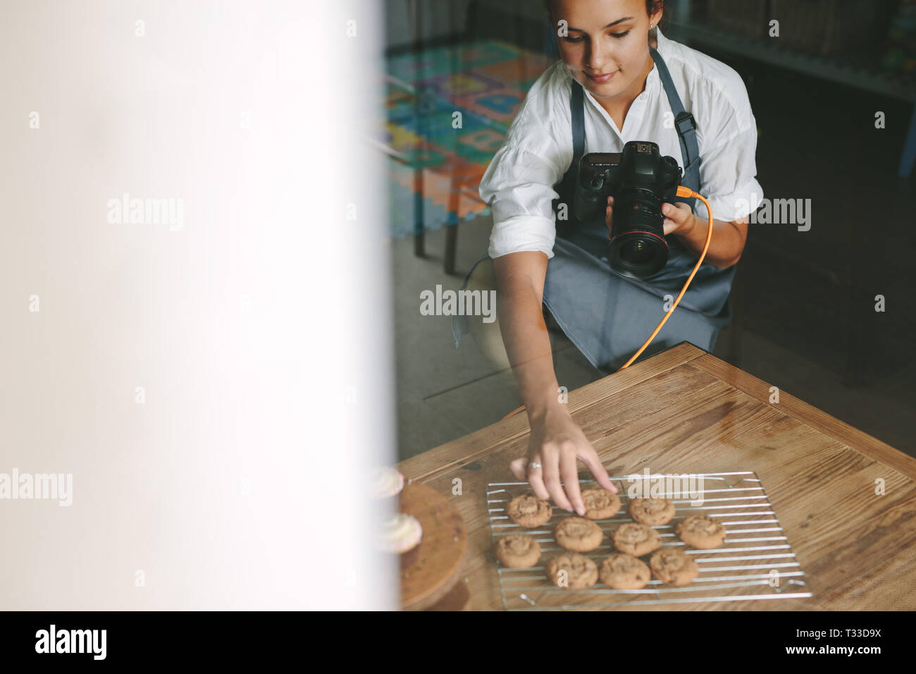 Femme chef à l'intérieur d'une cuisine disposant les cookies sur le grill avec caméra numérique en main. Femme en photographiant l'aire des pâtisseries dans la cuisine. Banque D'Images