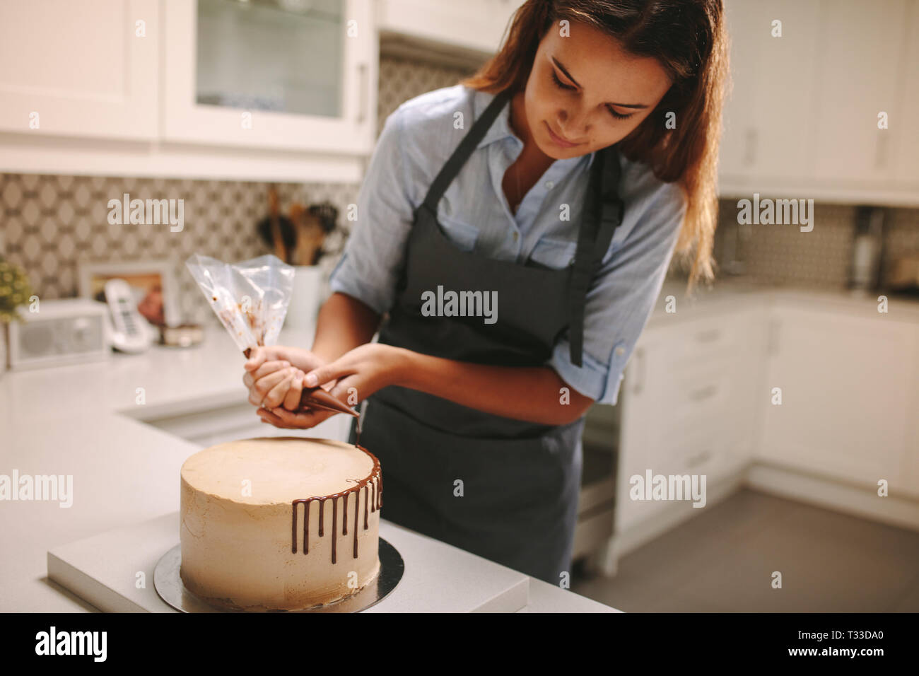 Pâtissier décore gâteau au chocolat glaçage. Gâteau sur comptoir de la cuisine avec les femmes chef decorating. Banque D'Images