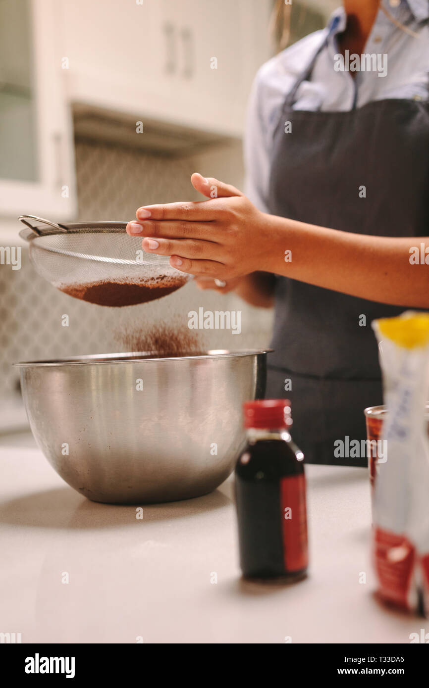 Close up of female chef pâtissier chocolat tamiser la farine dans un bol pour faire la pâte dans la cuisine. La farine tamisage femme tout en préparant le gâteau. Banque D'Images