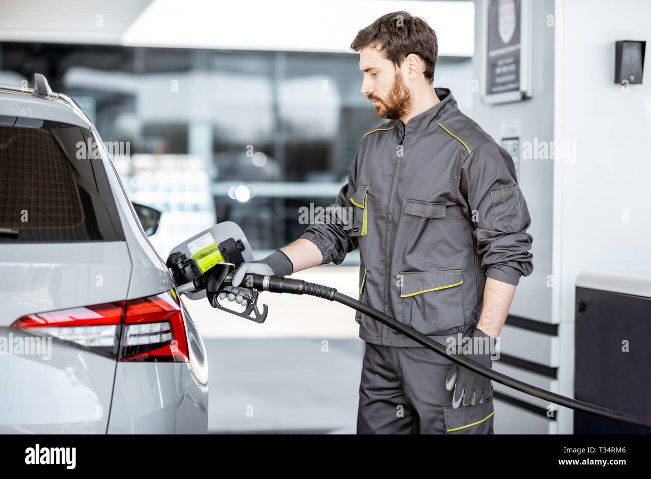 Station de gaz en travailleur de ravitaillement vêtements, voiture de luxe avec la tenue de l'essence à la station pistolet de remplissage Banque D'Images