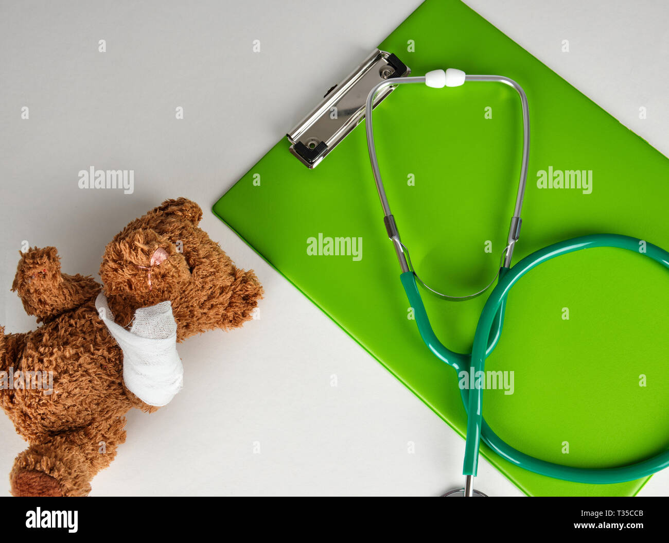 Stéthoscope médical et porte-papier vert sur fond blanc, à côté d'un ours en peluche, pédiatrie concept Banque D'Images