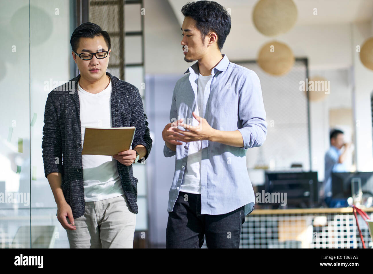 Deux jeunes collègues asiatiques discuter affaires tout en marchant dans le bureau. Banque D'Images