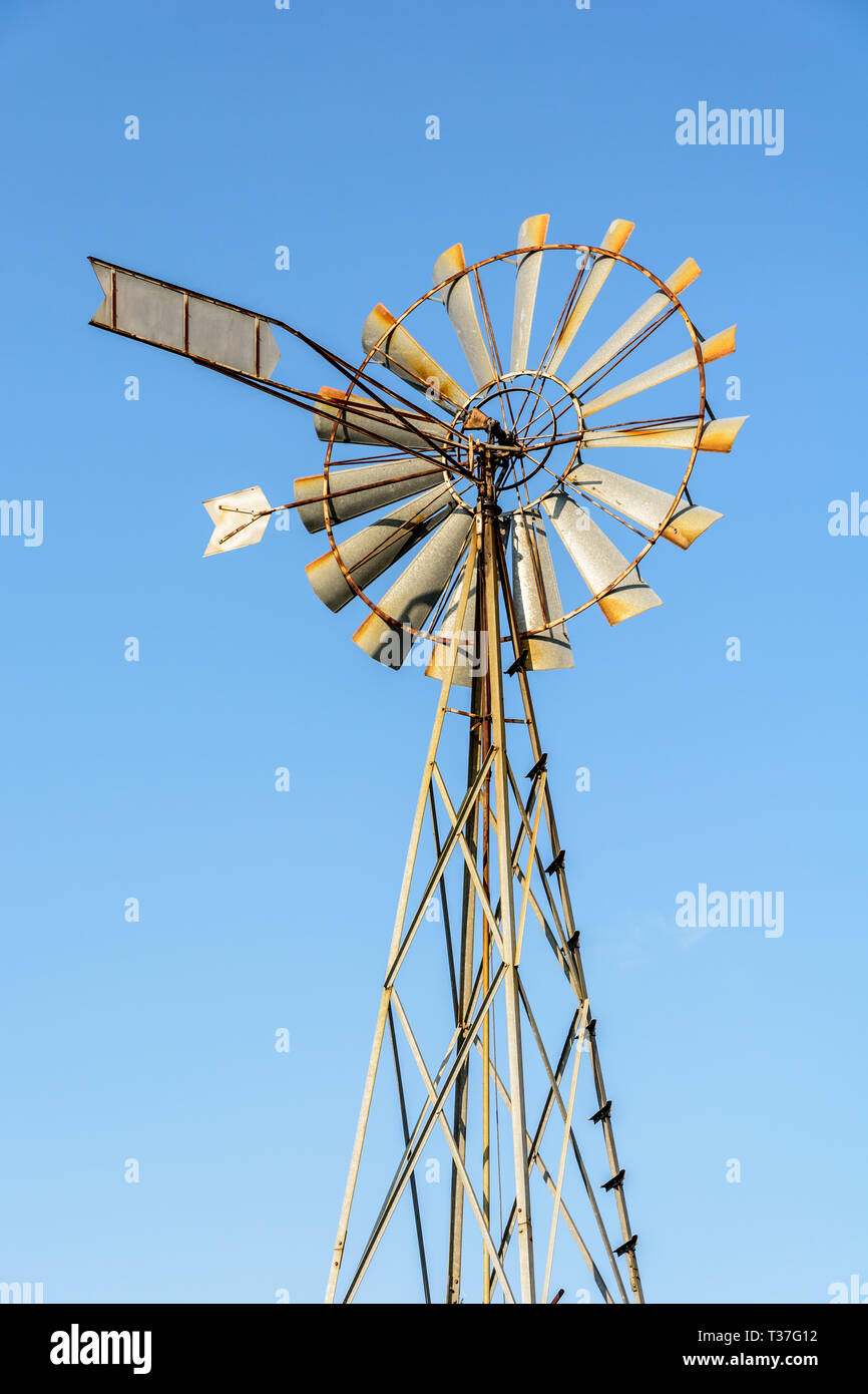 Low angle view of an old-fashioned, multi-lames, metal pompe éolienne au sommet d'un pylône en treillis contre le ciel bleu. Banque D'Images