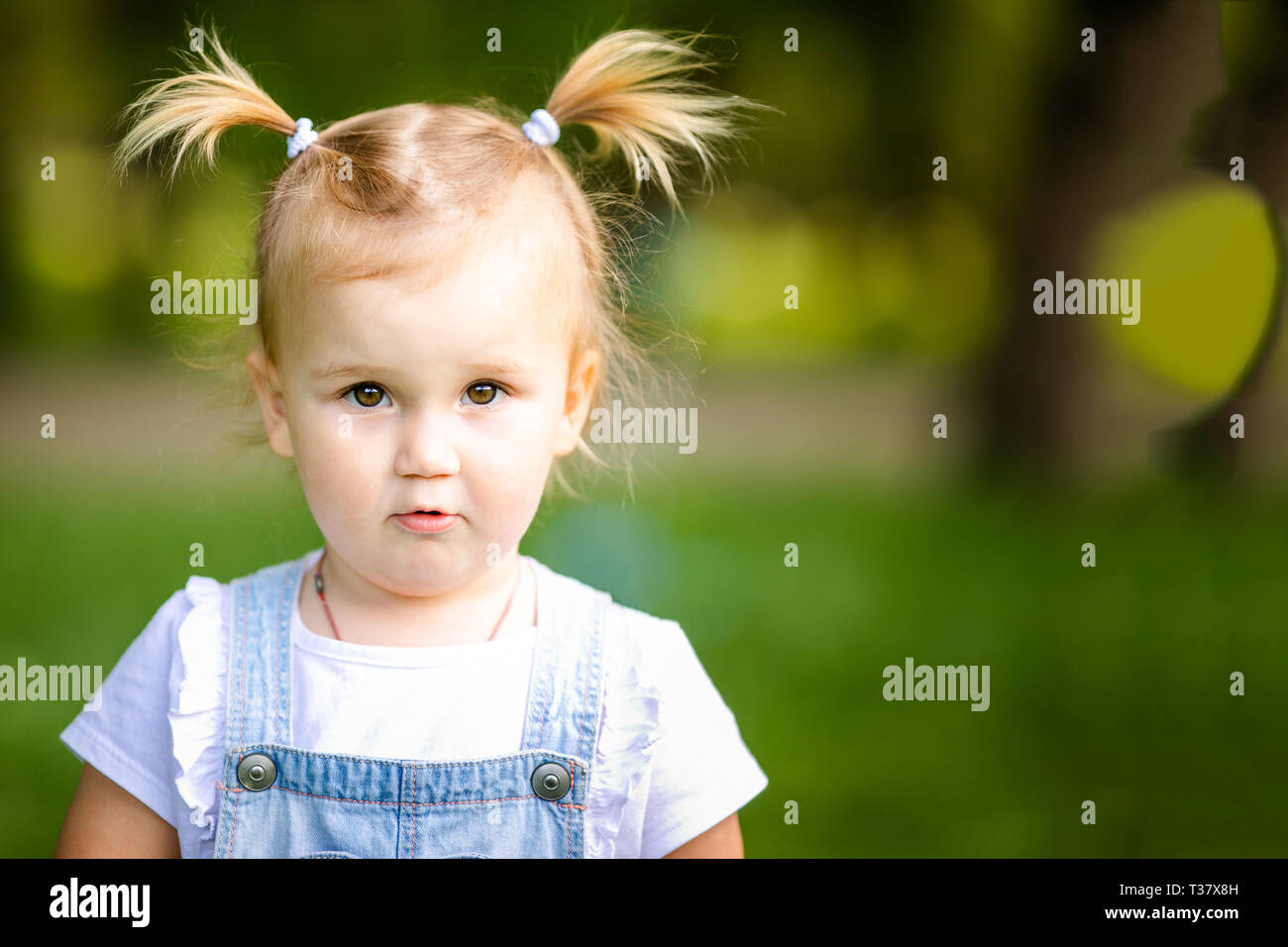 Happy Funny Blond Bebe Fille Avec Deux Petites Tresses En Blanc T Shirt Et Jeans Bodykit Assis Sur Fond D Herbe Verte Photo Stock Alamy