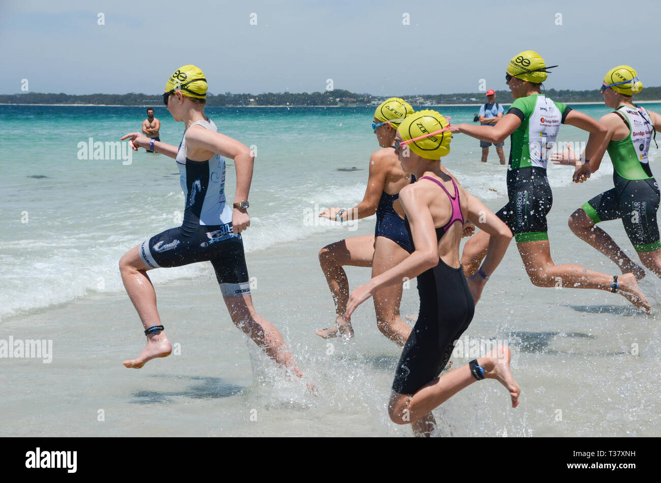 Groupe de femmes athlètes triathlon courir dans les vagues pour nager partie de la race, de l'eau splash et les athlètes d'exécution. Plage de triathlons exécuter int Banque D'Images