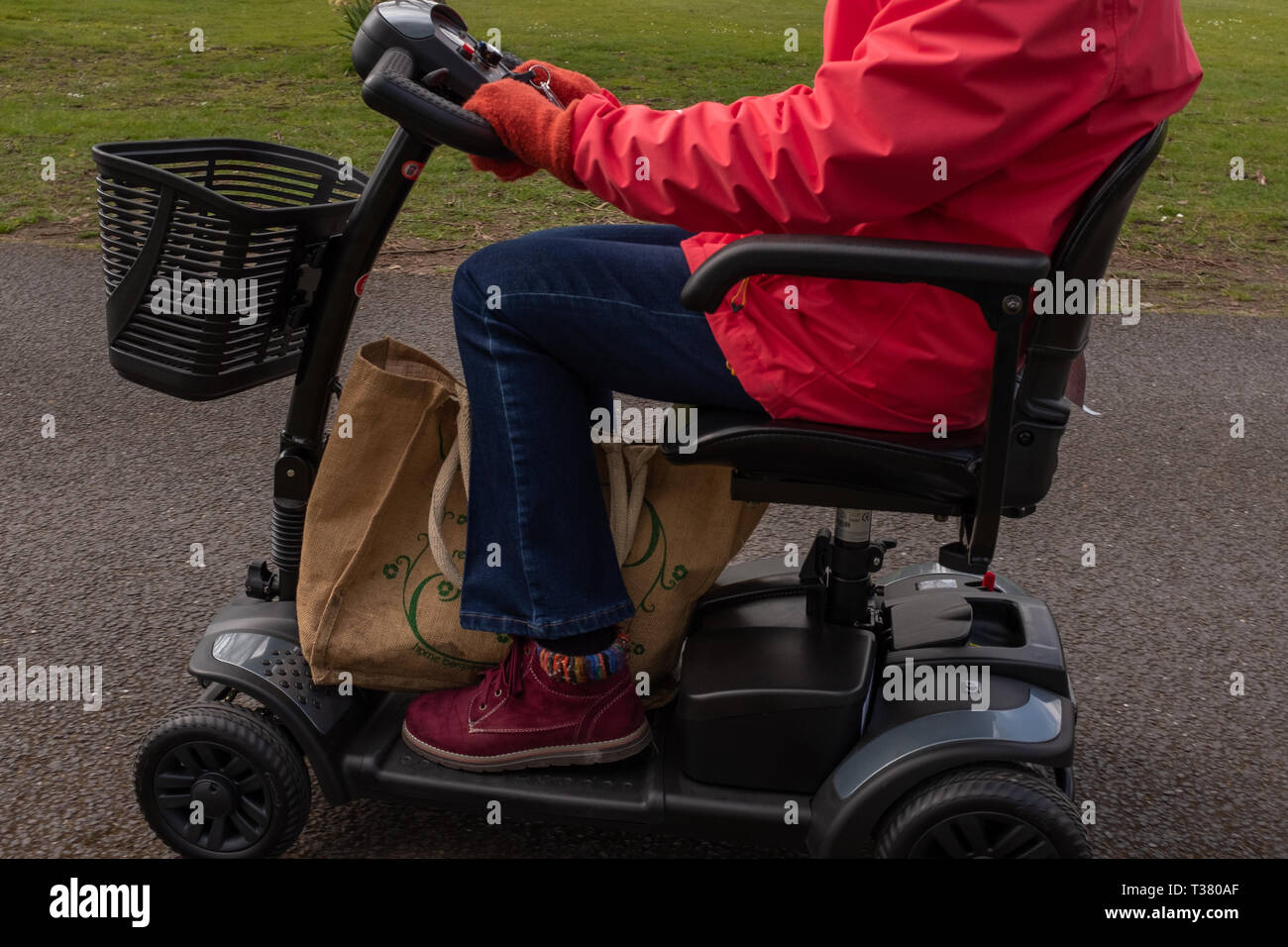 Un coup de côté sur une vieille dame dans un manteau rouge vivre la liberté d'un scooter de mobilité électrique, des épaules vers le bas Banque D'Images