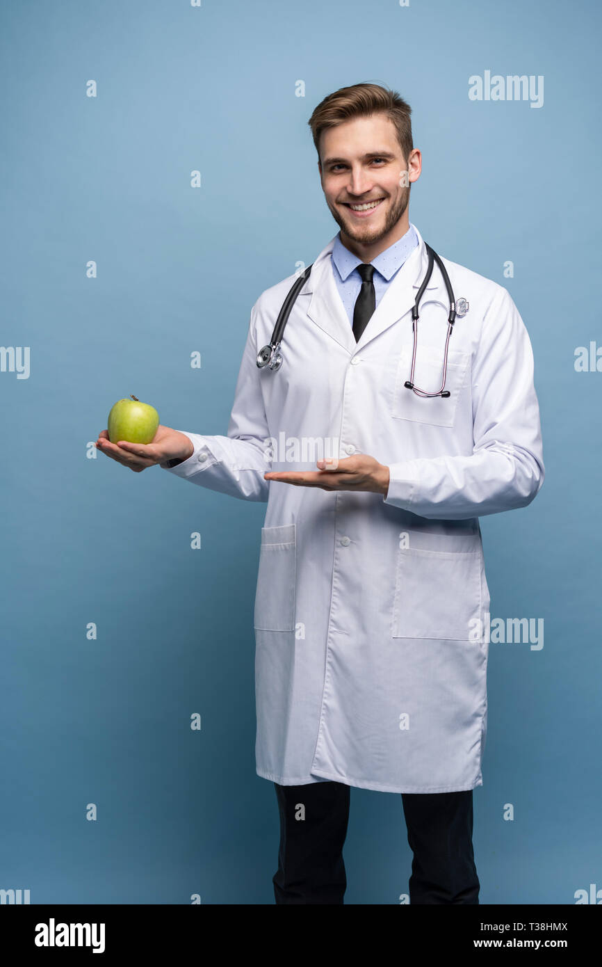 Portrait of young male Doctor Holding Green Apple. Isolé sur bleu clair. Banque D'Images