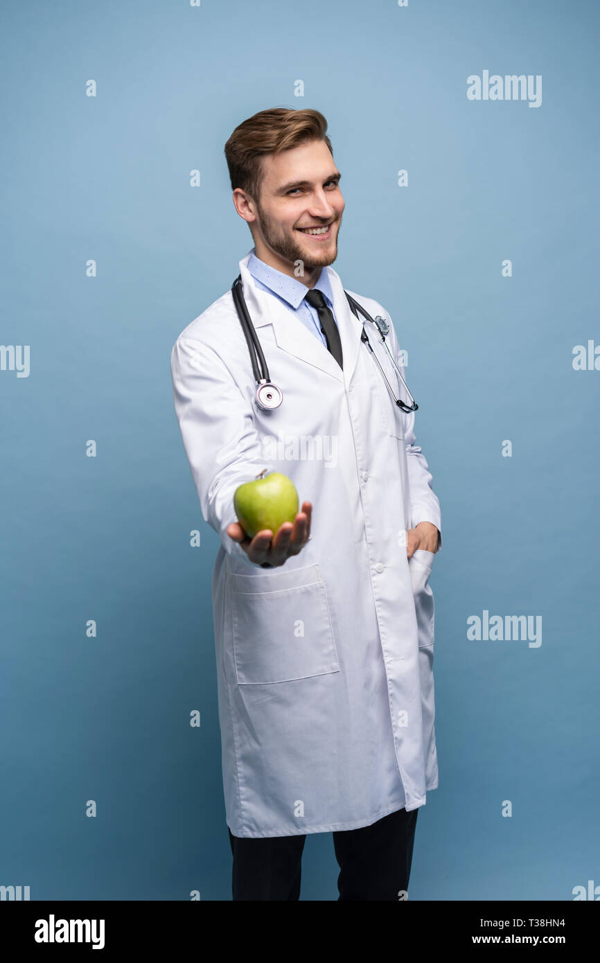 Portrait of young male Doctor Holding Green Apple. Isolé sur bleu clair. Banque D'Images