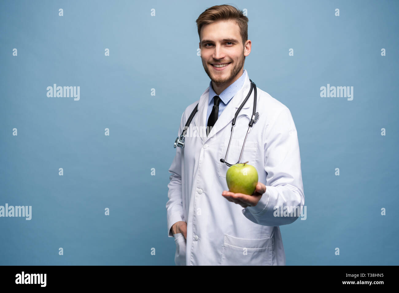 Portrait of young male Doctor Holding Green Apple. Isolé sur bleu clair. Banque D'Images