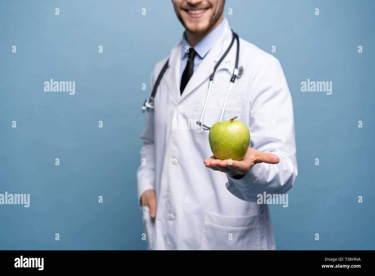 Portrait of young male Doctor Holding Green Apple. Isolé sur bleu clair. Banque D'Images