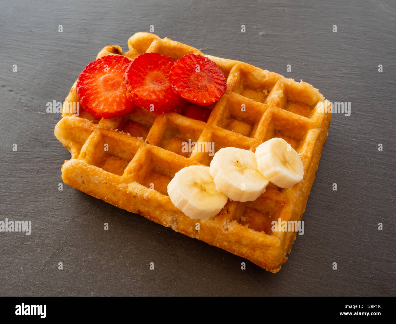 Une gaufre belge avec des morceaux de banane et de fraise sur une plaque en ardoise Banque D'Images