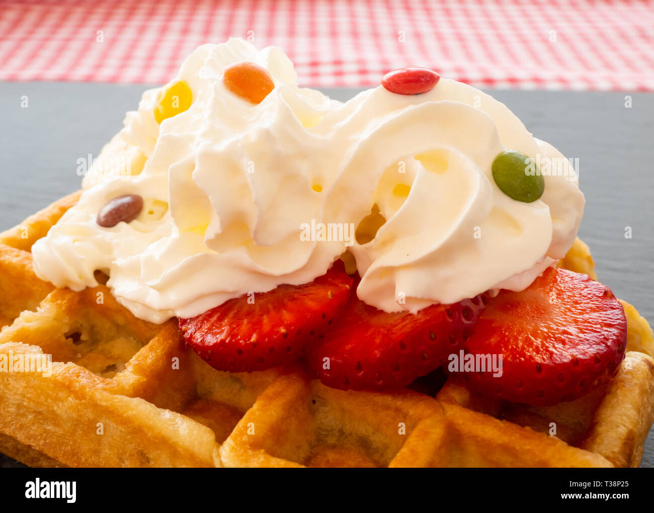 Une gaufre belge avec de la crème et des chocolats colorés plus de morceaux de fraises sur une plaque en ardoise Banque D'Images