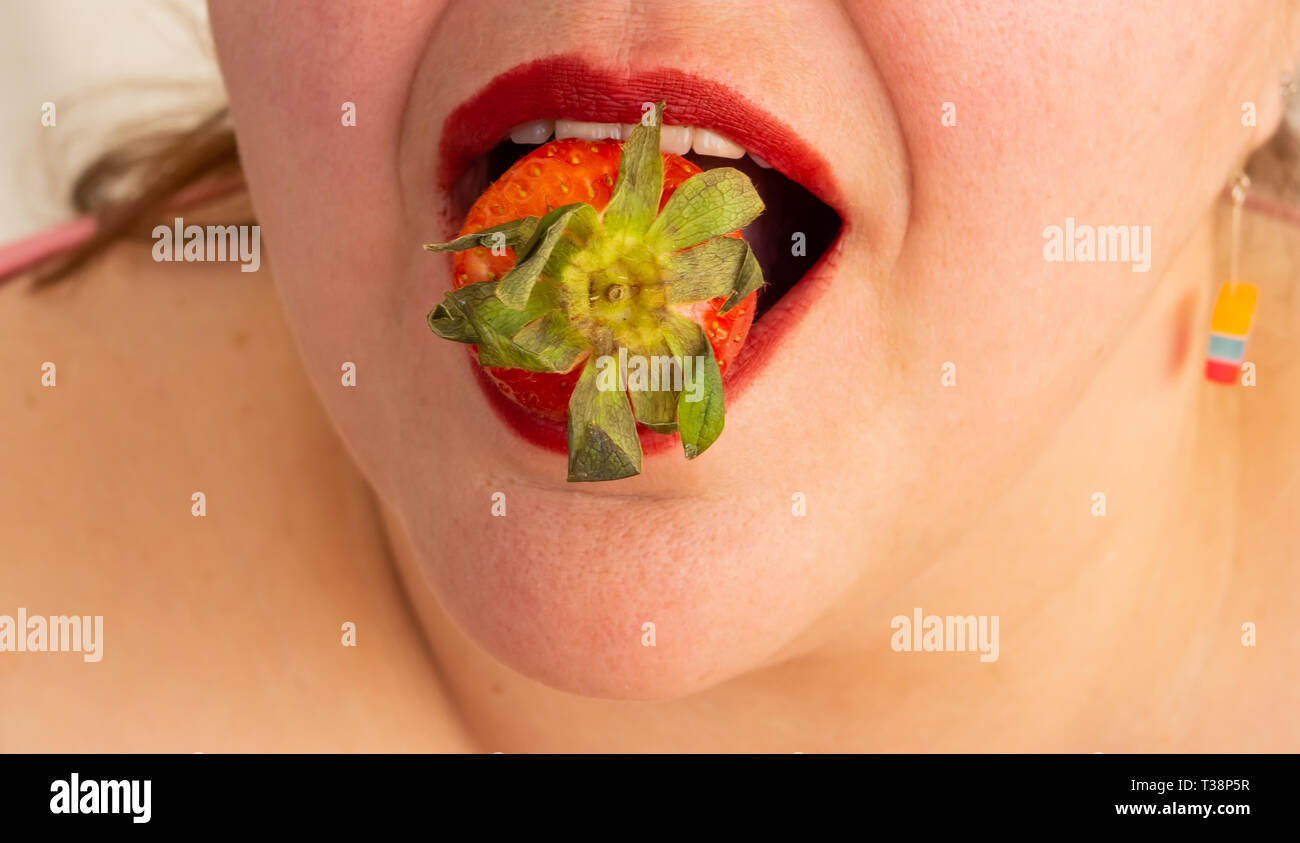 Une femme adulte avec les ongles et les lèvres rouges de manger une fraise Banque D'Images