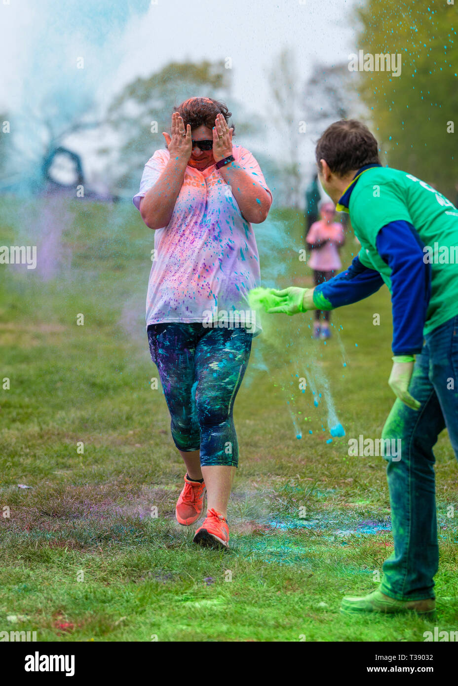 Femelle adulte walker avec les mains sur son visage se couvrir de peinture sur Macmillan Cancer 5K fun run de couleur. Banque D'Images