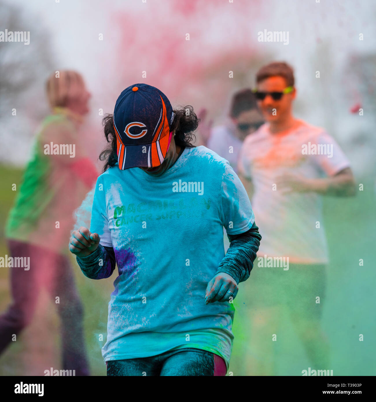 Coureuse noir avec capuchon à la recherche vers le bas et recouverte de peinture sur Macmillan Cancer 5K fun run de couleur. Banque D'Images